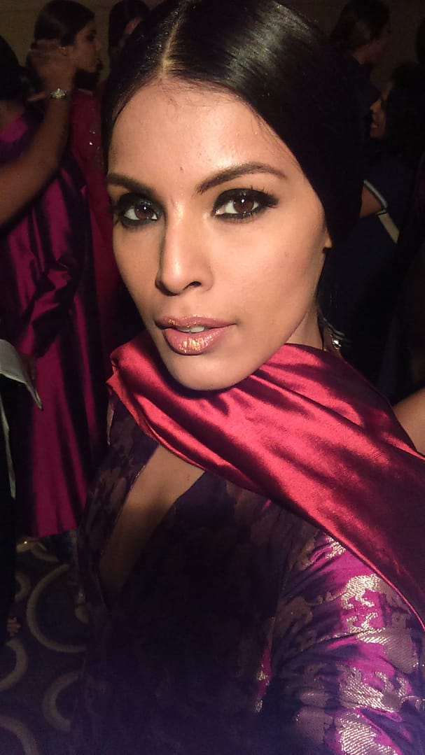 Runway model with sleek hair, bold smokey eyes, and metallic nude lips wearing a red draped outfit, styled by Cezenia Dias Makeup Artist in Goa and Mumbai for a fashion show.